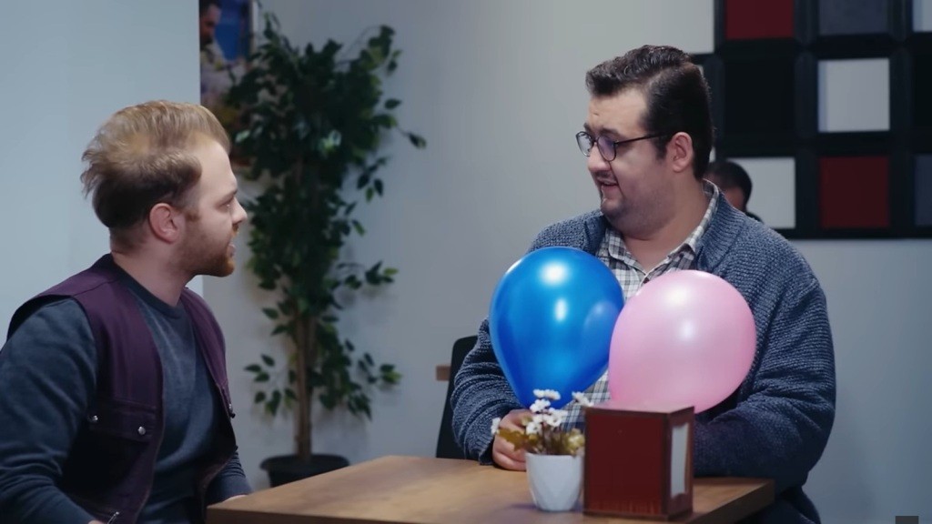 Scena w stołówce. Kirpi i Ibrahim siedzą przy stoliku. Ibrahim trzyma w rękach dwa balony.