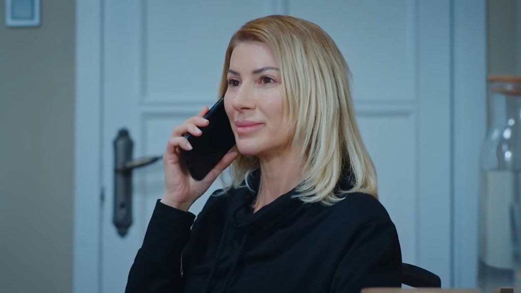 Isil rozmawia przez telefon. Uśmiecha się z zadowoleniem.