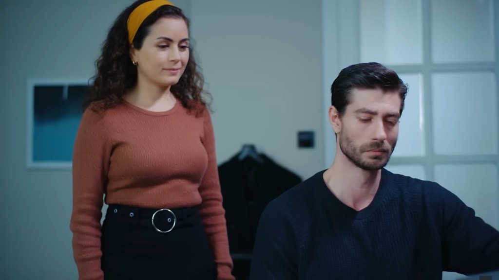 Aynur stoi za plecami Sinana i uśmiecha się delikatnie.