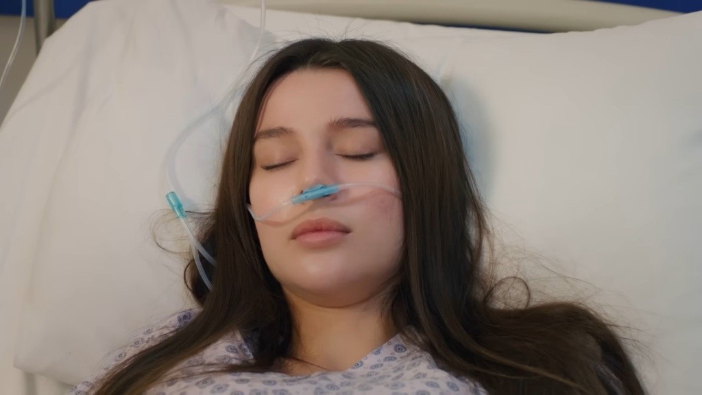 Zbliżenie na twarz nieprzytomnej Zeynep, leżącej na łóżku szpitalnym.