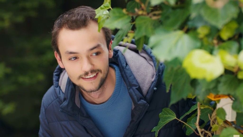 Alper wygląda zza zarośli.