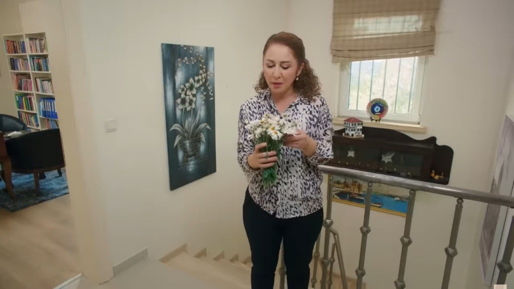 Hulya trzyma w rękach wazon ze stokrotkami.