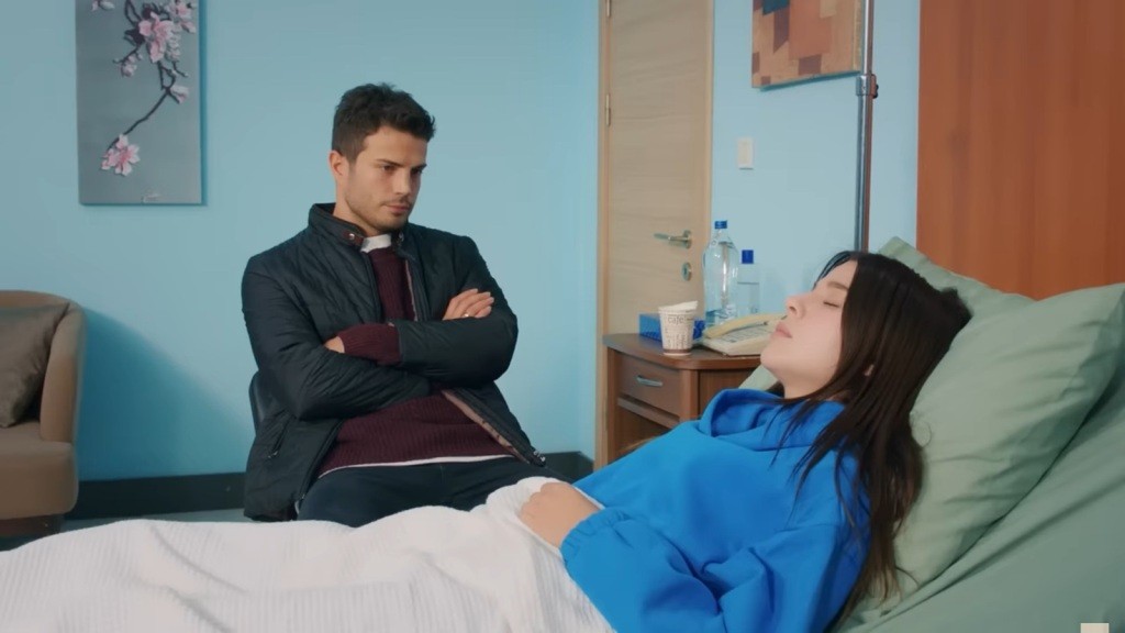 Ege siedzi ze skrzyżowanymi na piersi rękami, patrząc na śpiącą Zeynep.
