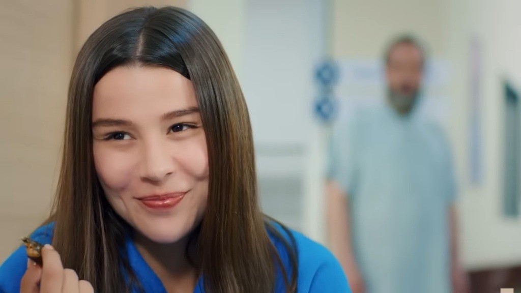 Zeynep uśmiecha się. Za jej plecami widać męską sylwetkę.