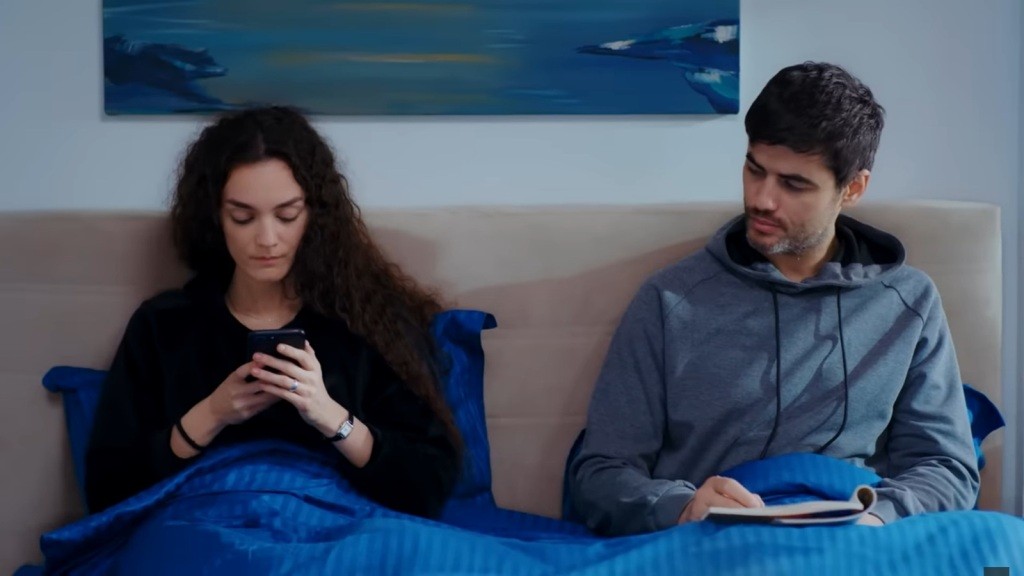 Nana i Poyraz leżą w łóżku. Ona wpatruje się w ekran telefonu, a on patrzy na nią.