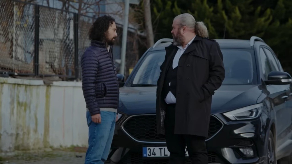 Semih rozmawia z Sedatem przed samochodem.