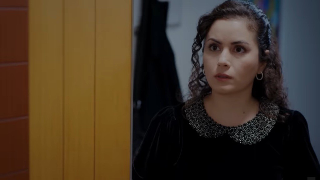 Aynur stoi przy otwartych drzwiach, a na jej twarzy maluje się zaskoczenie.