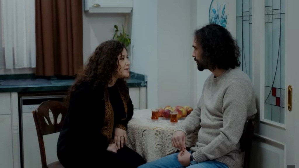 Cansel i Semih rozmawiają, siedząc przy stoliku w kuchni.