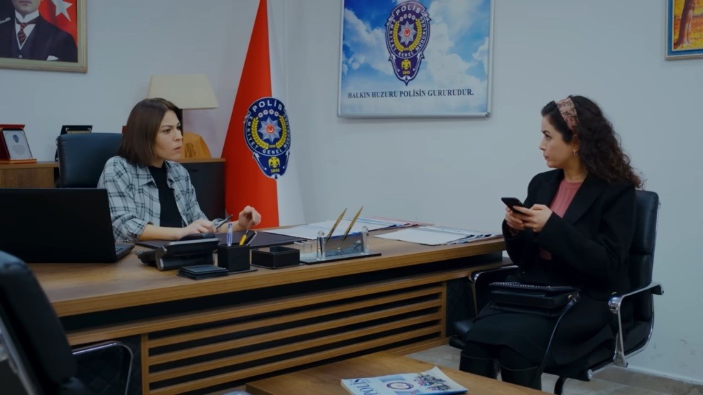 Kara i Aynur przy biurku. Aynur trzyma telefon w rękach.