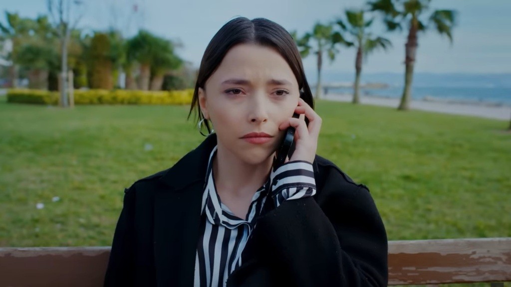 Ezgi siedzi na ławce na wybrzeżu. Rozmawia przez telefon.