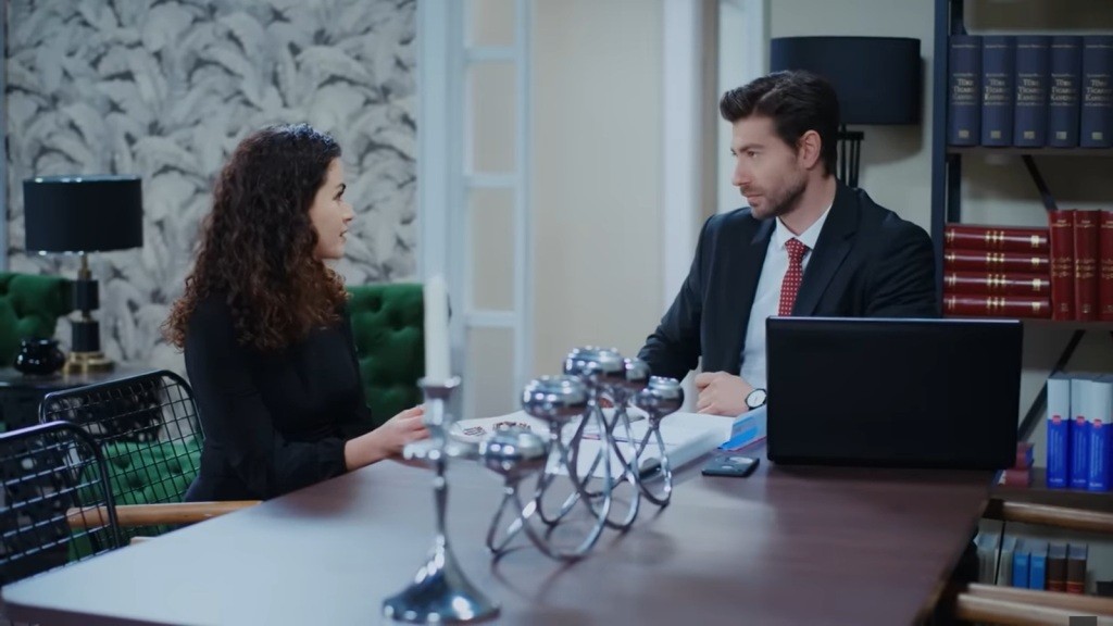 Aynur i Sinan siedzą przy stole w jego domu.
