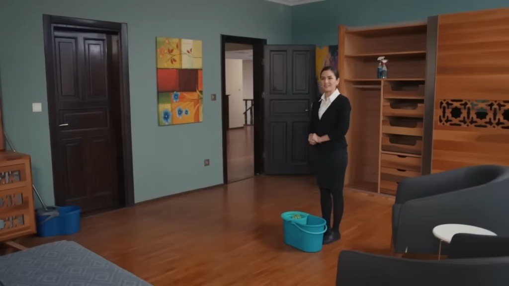 Aynur stoi przy wiadrze z mopem w wysprzątanym pokoju Nany.
