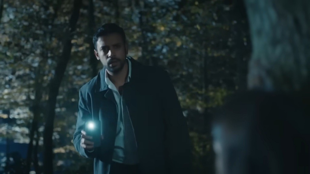Koray oświetla sobie drogę przez las telefonem.