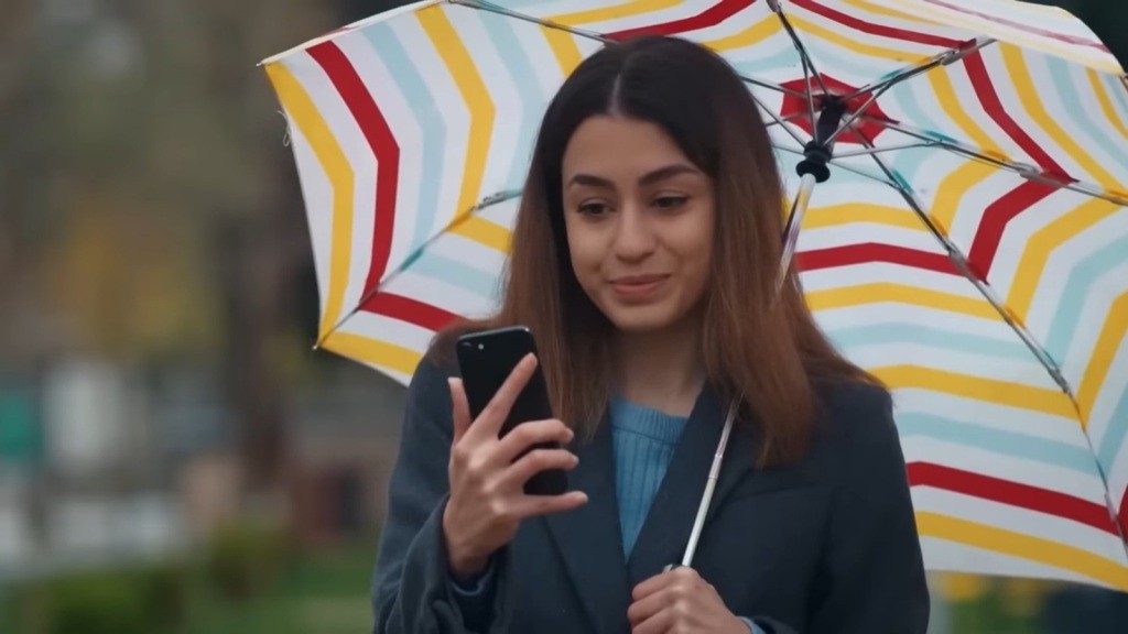 Pinar trzyma parasolkę w jednej ręce, a w drugiej dzierży telefon.