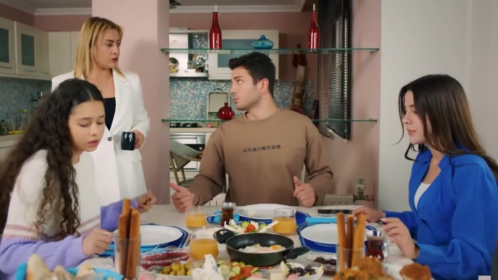 Melodi, Ege i Zeynep jedzą śniadanie. Obok, z kubkiem w ręku, stoi Belkis.