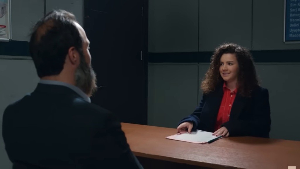 Melis siada przed Ragipem w pokoju przesłuchań.