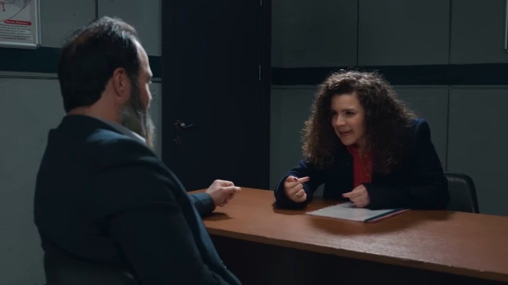 Melis siedzi naprzeciwko Ragipa w pokoju przesłuchań.