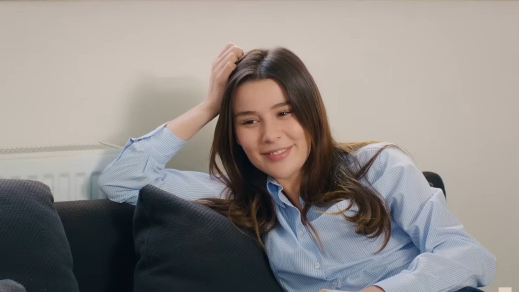 Zeynep uśmiecha się, siedząc na kanapie.
