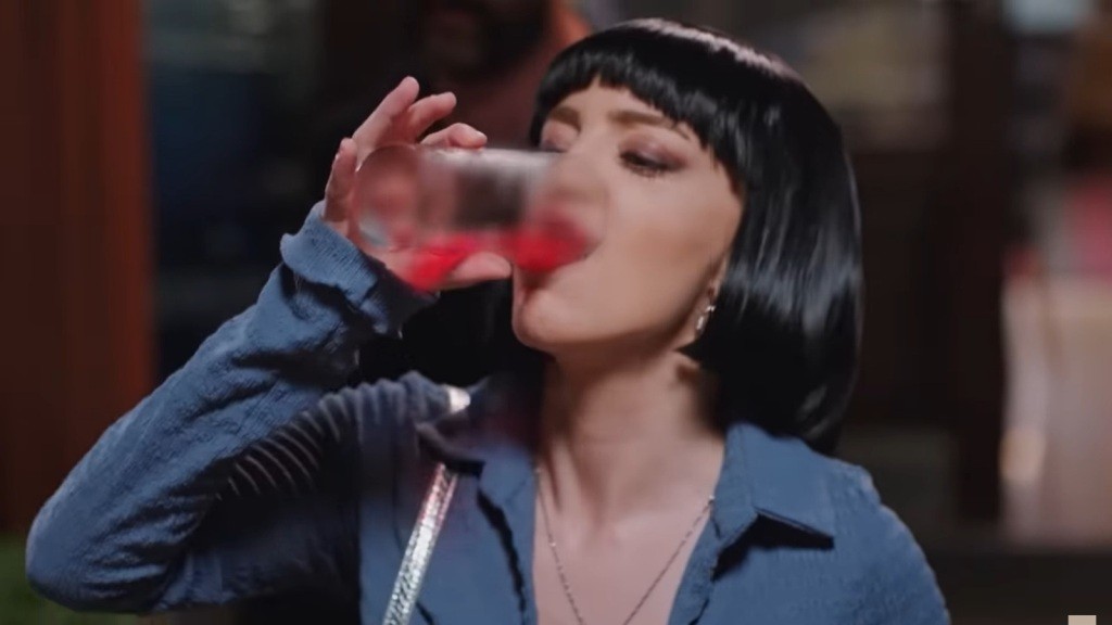 Seda przechyla szklankę z drinkiem.