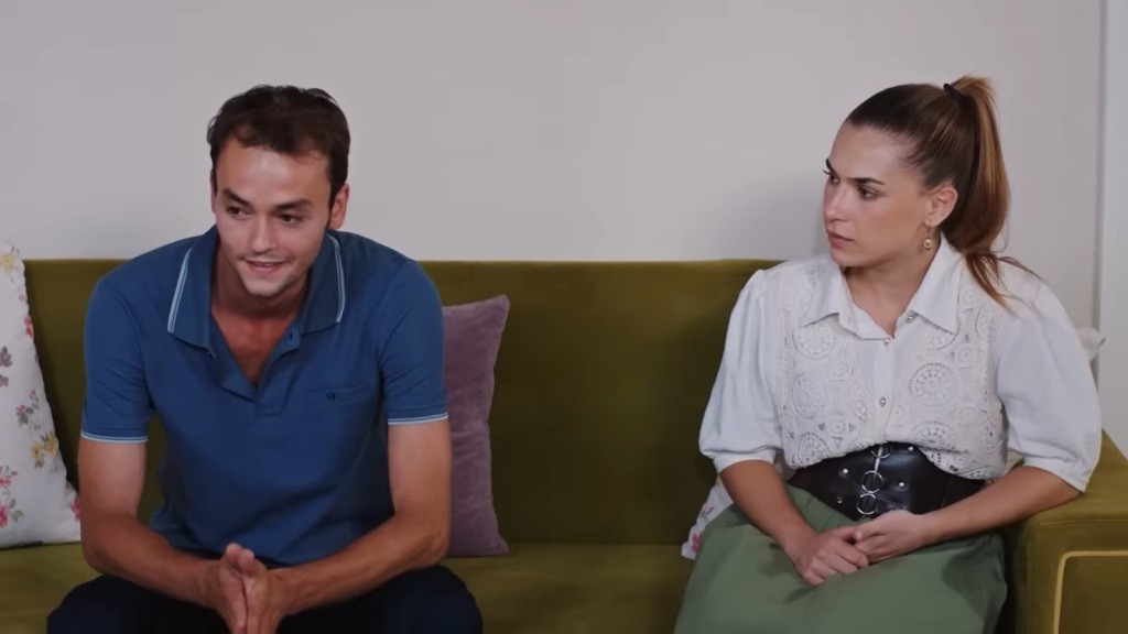 Alper i Sila siedzą na kanapie. On uśmiecha się pod nosem, a ona przygląda mu się uważnie.