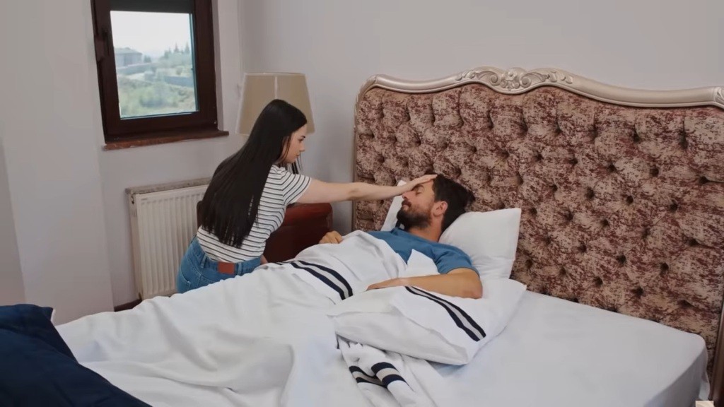 Bahar siedzi przy łóżku śpiącego Kuzeya. Dotyka ręką jego czoła.