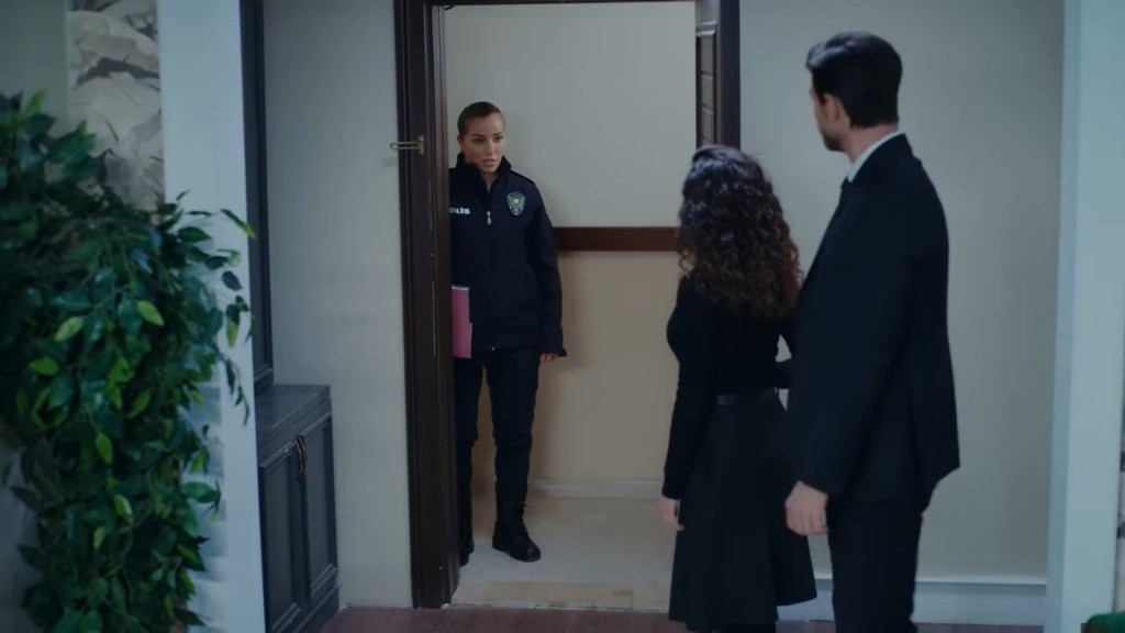 Przed wejściem do mieszkania Sinana stoi policjantka. Aynur i Sinan stoją przy drzwiach.