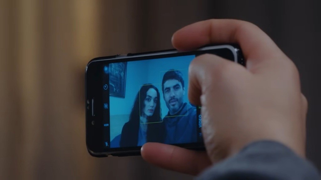 Zbliżenie na ekran telefonu Poyraza, na którym wyświetla się podgląd z przedniej kamery. Widać na nim pozujących do selfie Poyraza i Nanę.