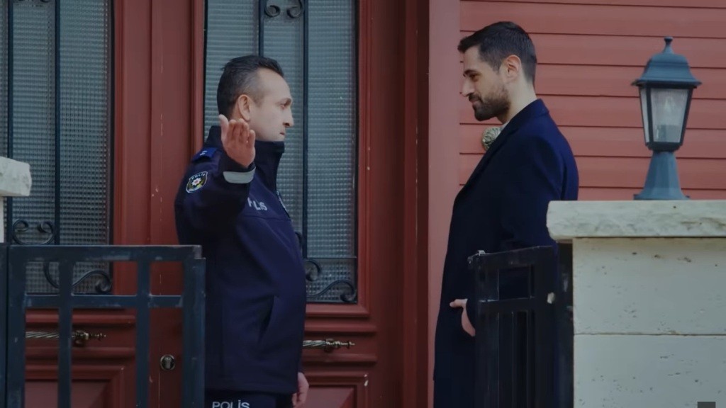 Policjant Rustem, stojąc z Atakanem twarzą w twarz, wskazuje ręką na furtkę.