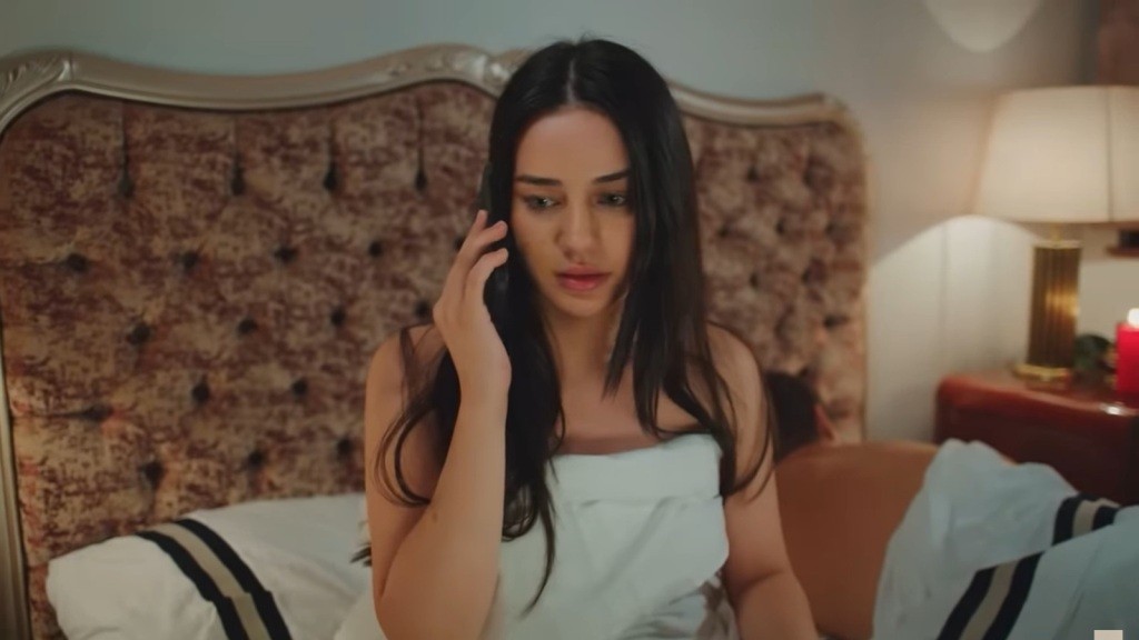 Bahar rozmawia przez telefon. Obok, w łóżku, śpi Kuzey.