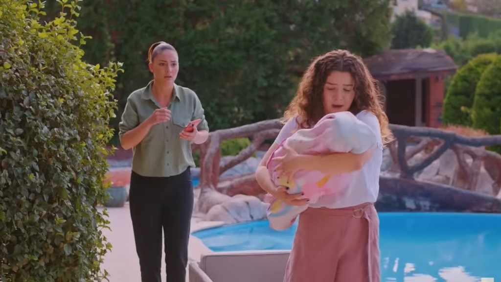 Melis trzyma dziecko na rękach. Yildiz stoi za jej plecami, patrząc z niedowierzaniem.