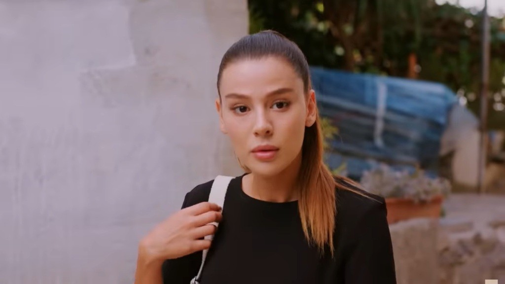 Zeynep patrzy z zaintrygowaniem, trzymając się za pasek torebki.