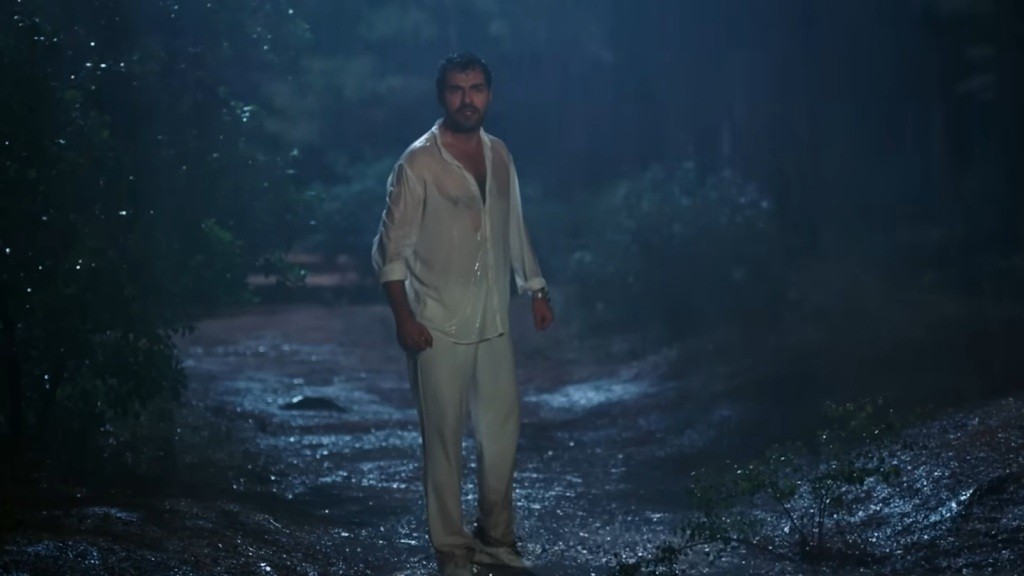 Halil stoi w strugach deszczu na leśnej drodze. Scena rozgrywa się w nocy.