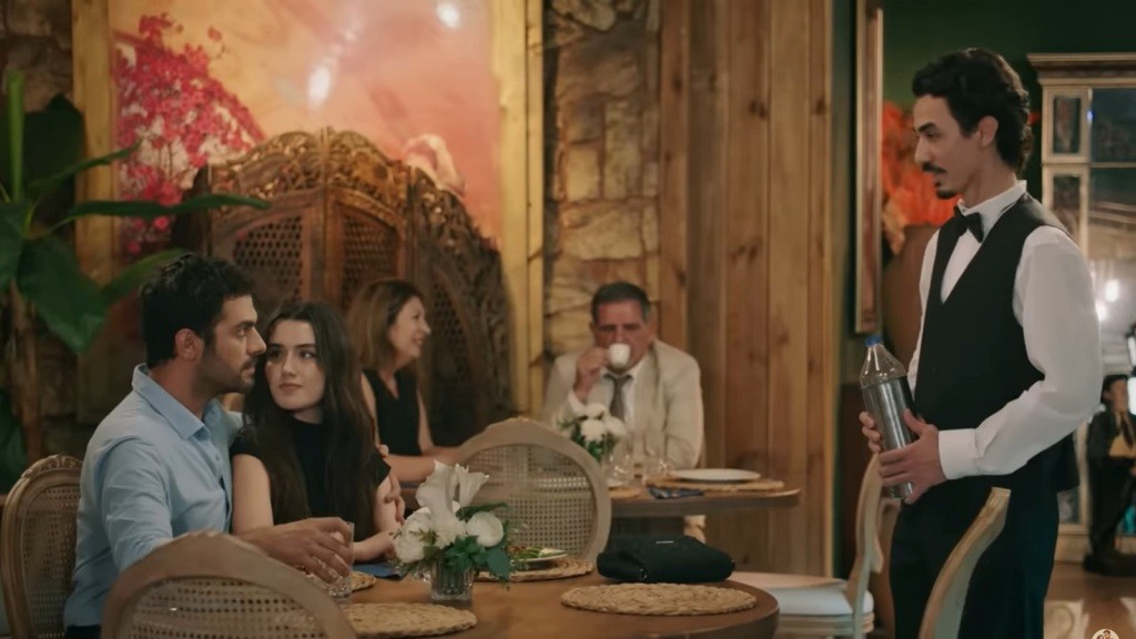 Scena w restauracji. Halil obejmuje Zeynep, patrząc groźnie na kelnera, stojącego przy stoliku.
