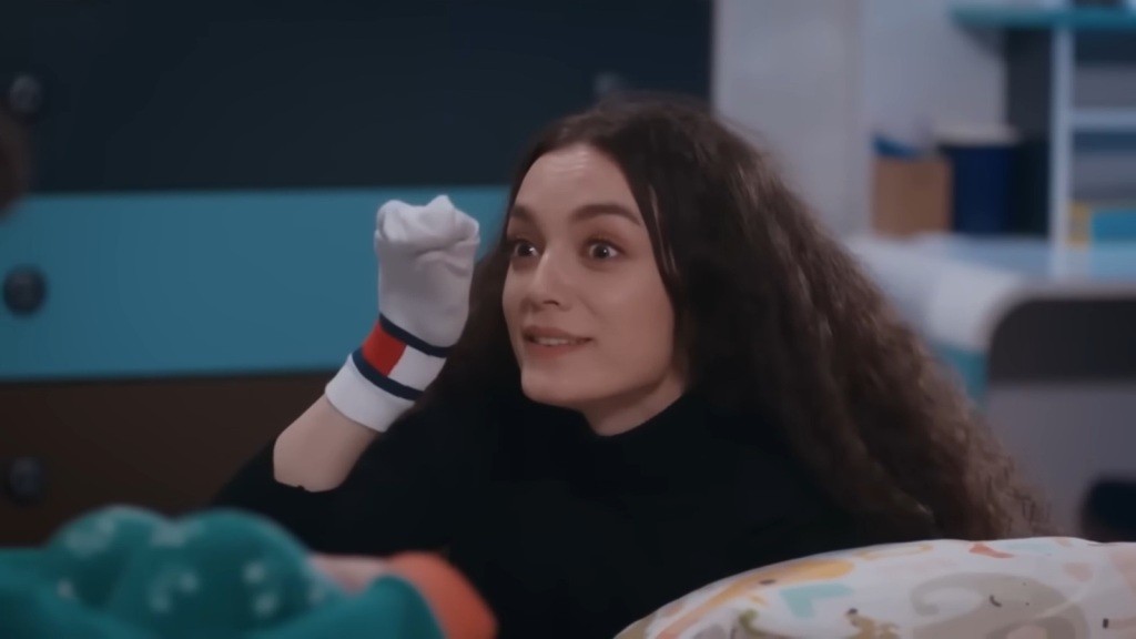 Nana ma założoną skarpetę na rękę i próbuje rozśmieszyć Yusufa.