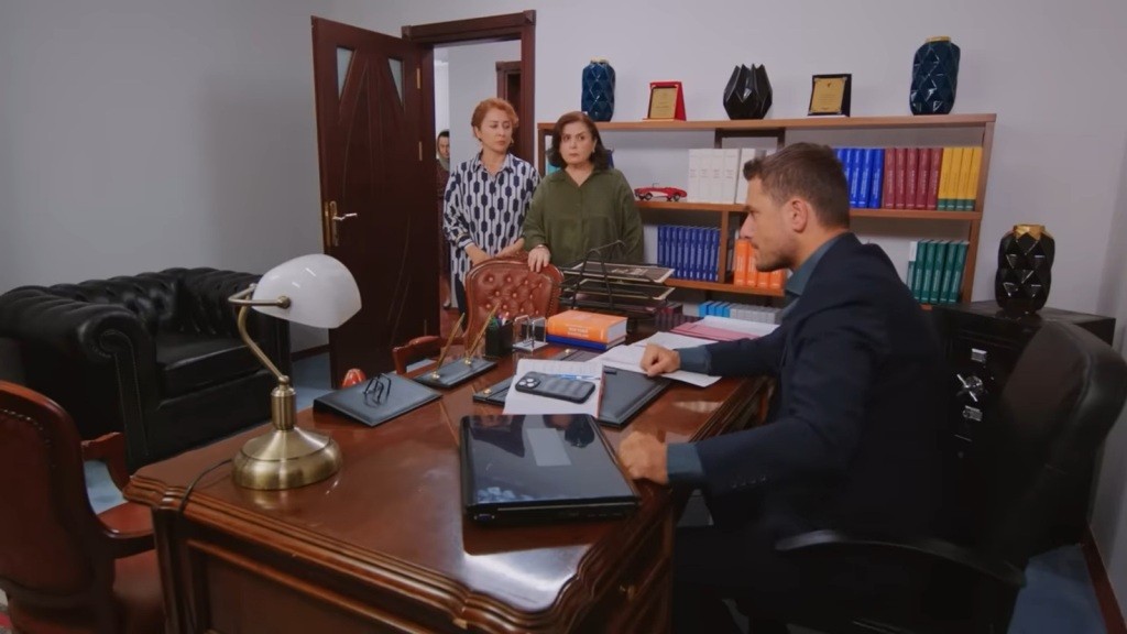 Kuzey siedzi przy biurku, zaciskając pięści. Przed biurkiem stoją jego mama i siostra.