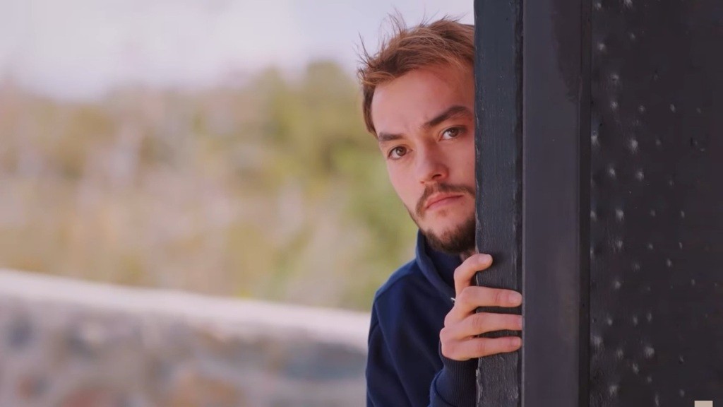 Alper wychyla głowę zza ogrodzenia, a jego twarz zdradza napięcie.