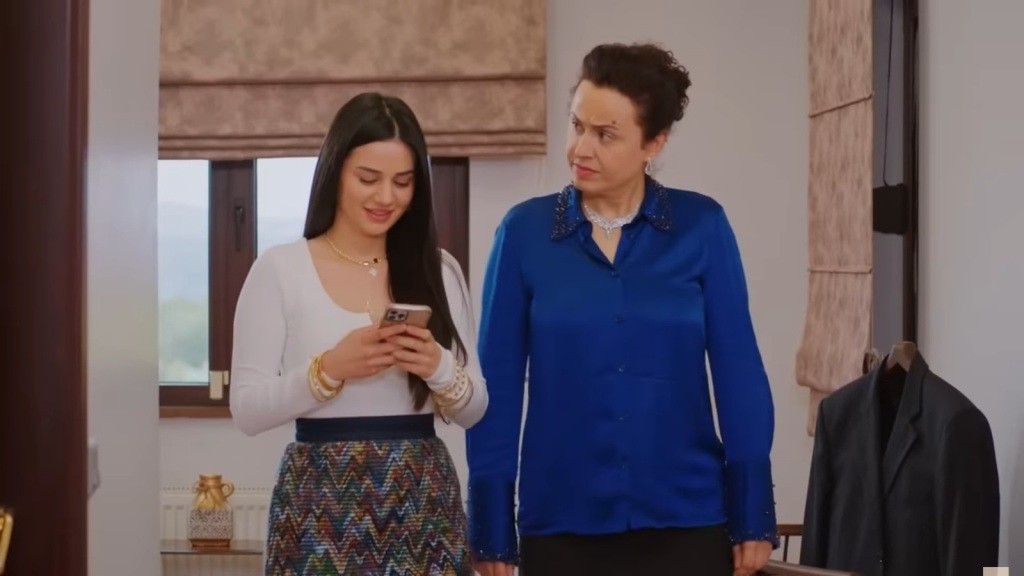 Bahar trzyma w rękach telefon i uśmiecha się. Obok niej idzie matka.