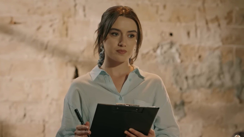 Zeynep trzyma w rękach notatnik i długopis.