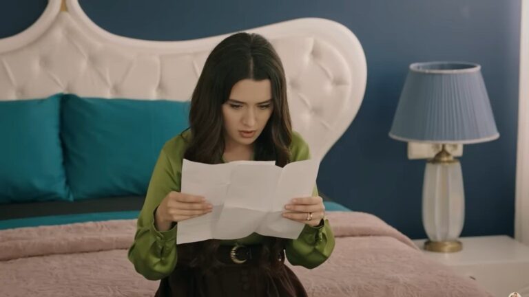 Zeynep siedzi na łóżku, w skupieniu porównując charakter pisma na dwóch listach. Jej twarz wyraża zaskoczenie.