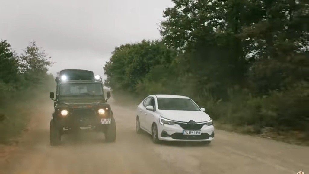 Halil ściga się z białym sedanem na piaszczystej drodze.