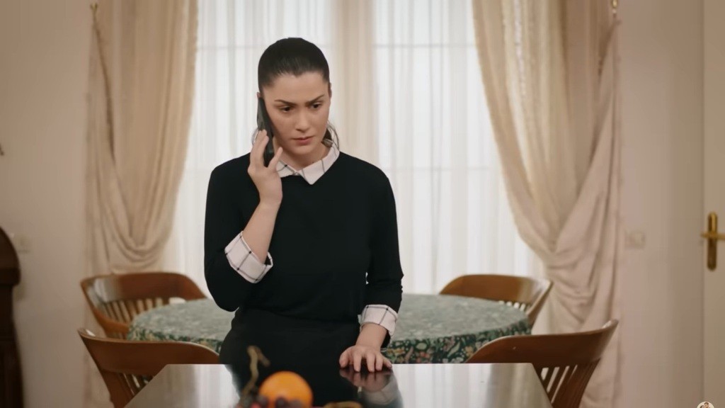 Arzu rozmawia przez telefon, opierając się o wyspę w kuchni. Sprawia wrażenie przejętej.