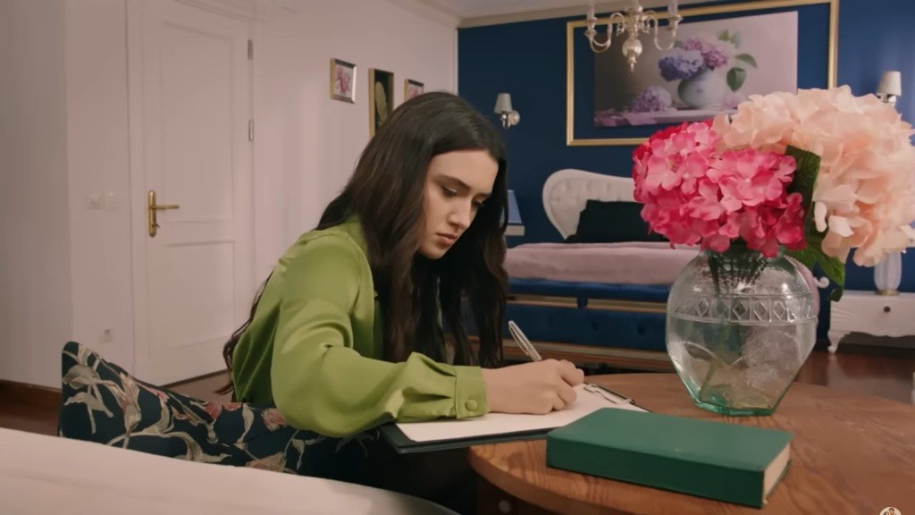 Zeynep siedzi przy stoliku w pokoju i pisze list.