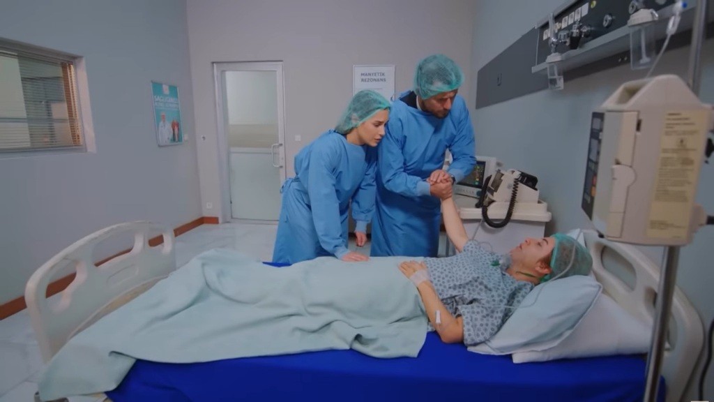 Kuzey i Sila w ubraniach ochronnych pochylają się na leżącą na szpitalnym łóżku Hulyą.