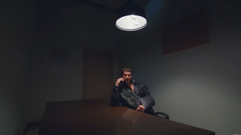 Cihan siedzi w pokoju przesłuchań i rozmawia przez telefon.