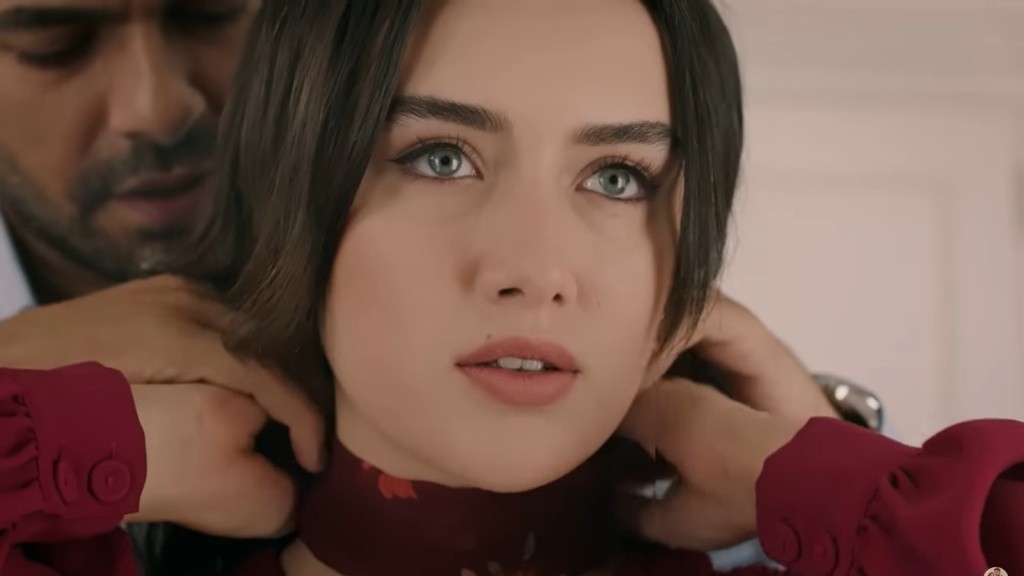 Halil pomaga Zeynep zawiązać apaszkę na szyi.