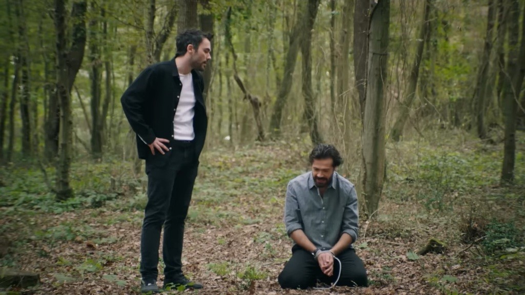 Wyczerpany Tekin upada na kolana w lesie. Hakan stoi obok niego.