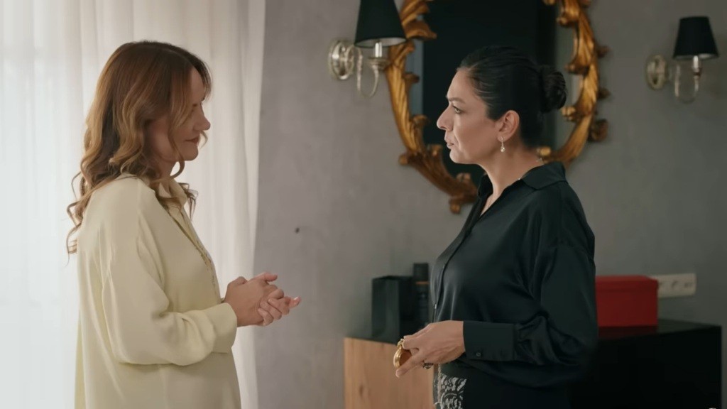 Tulay stoi przed Songul, trzymając w ręku złoty zegarek na łańcuszku.