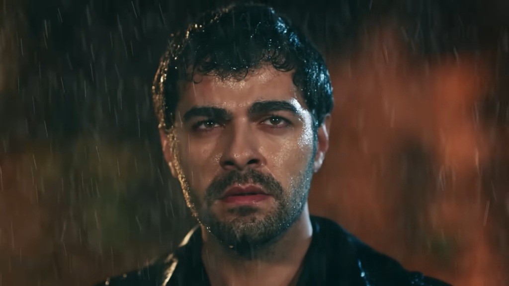 Halil stoi w strugach deszczu.