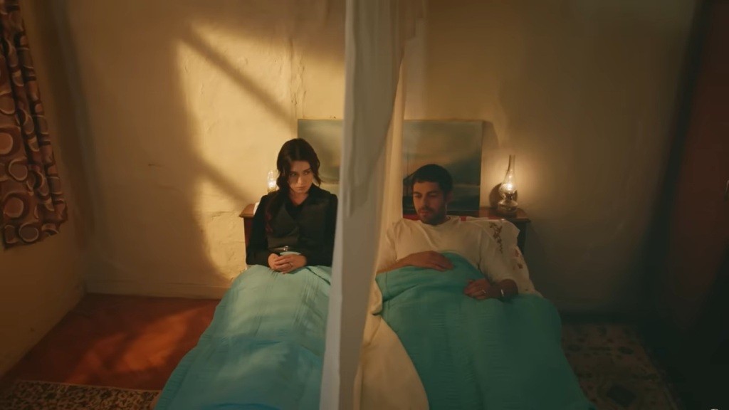 Zeynep i Halil leżą na jednym łóżku, ale rozdzieleni są kotarą z prześcieradła.