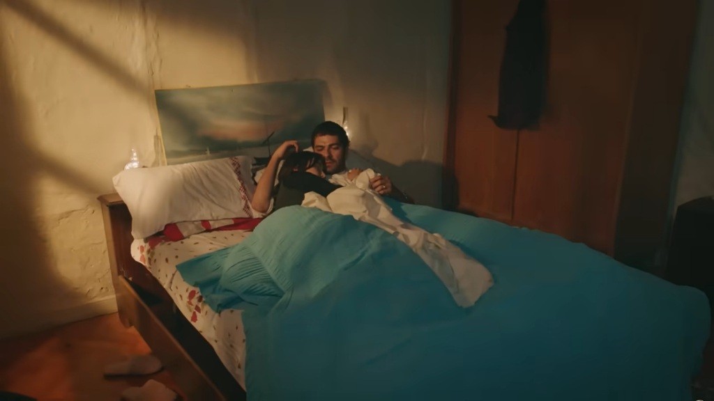 Zeynep obraca się na bok na łóżku, wtulając się w Halila.